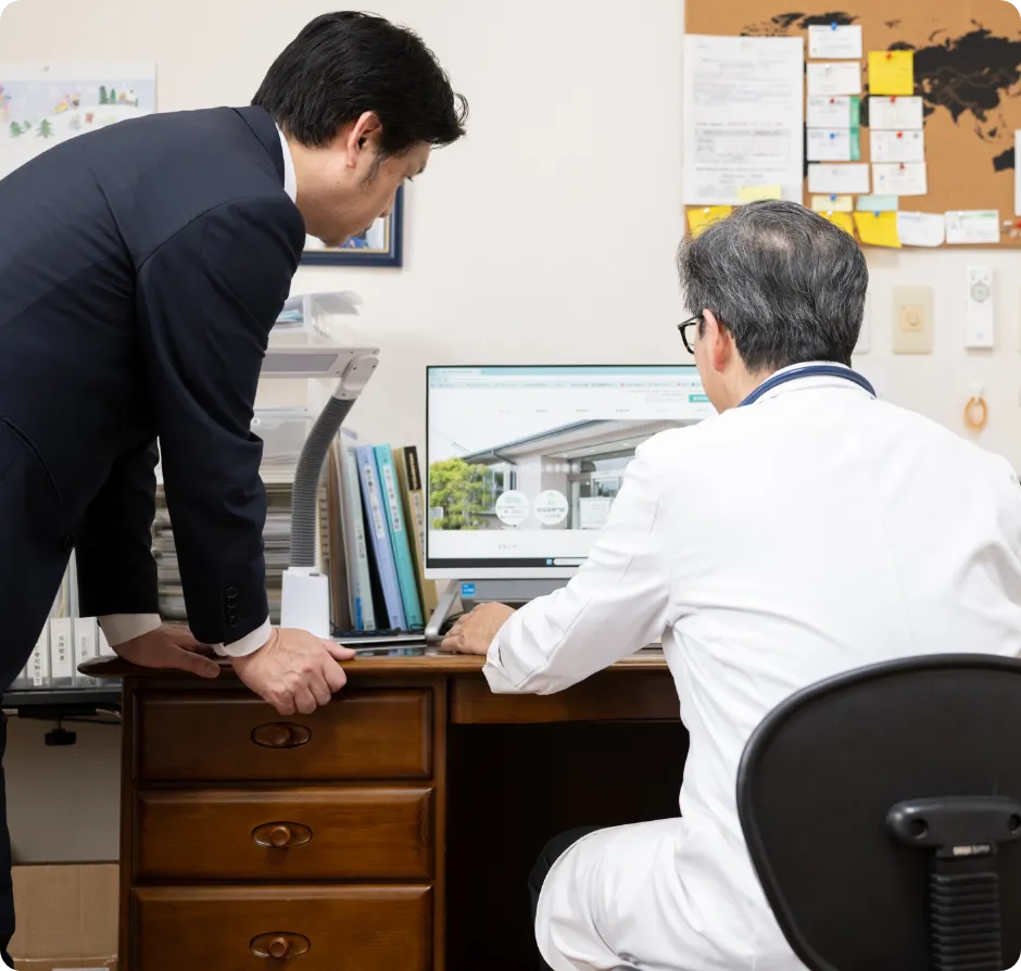 PCの画面を見ながら話し合う男性職員と医院の先生