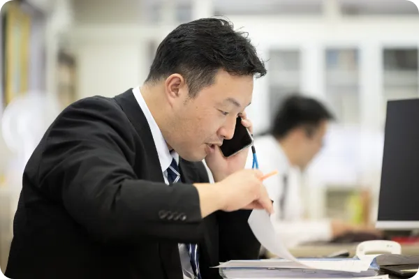 スマホで電話しながら書類をめくる男性職員