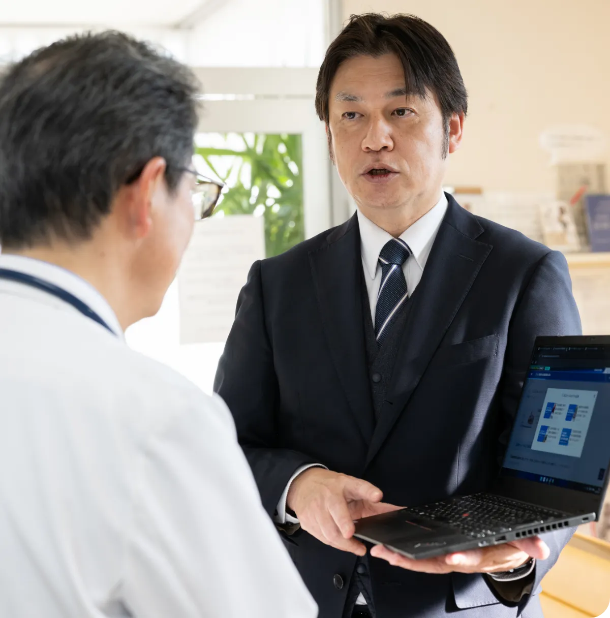 パソコンの画面を見せながら医師に説明する男性職員